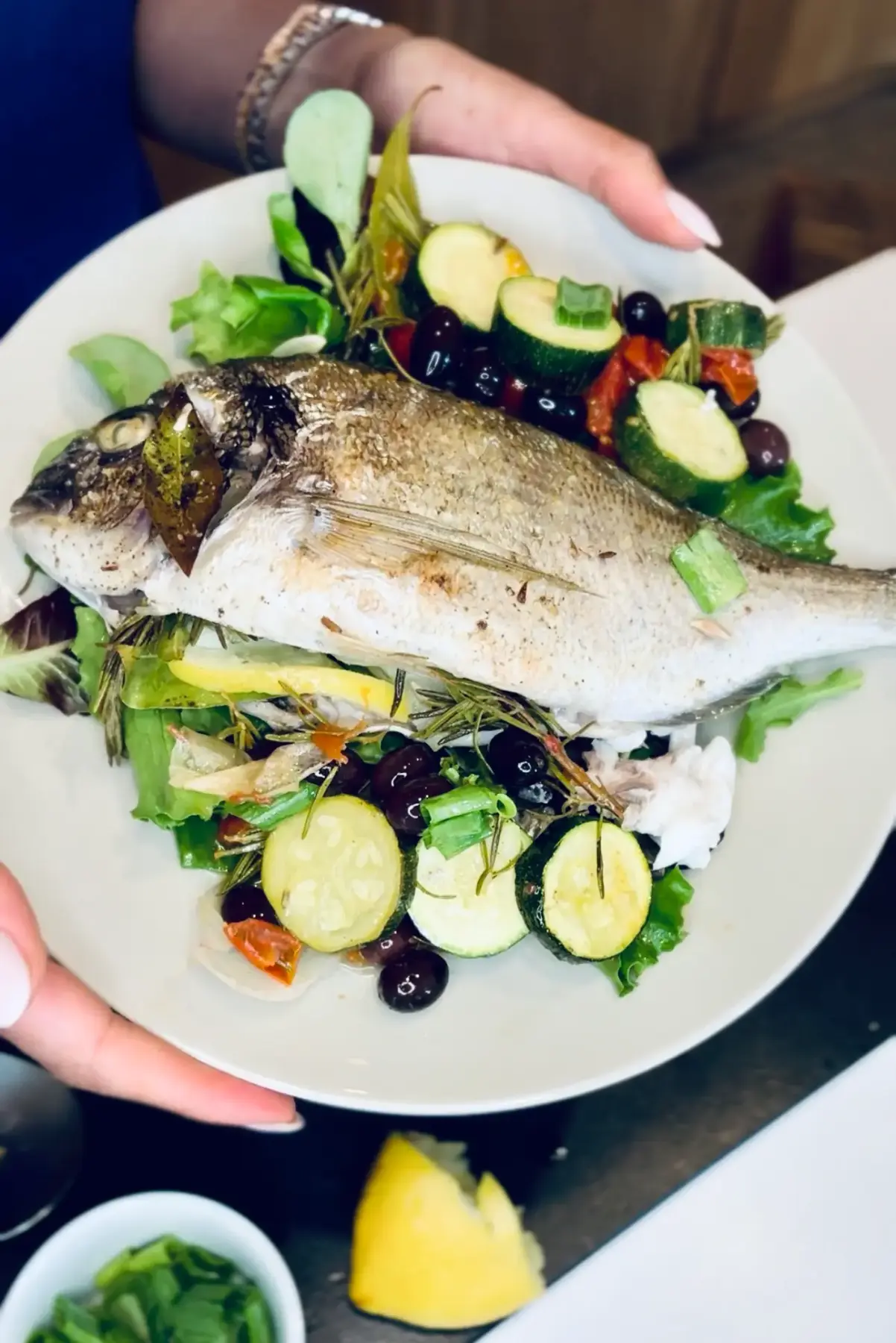 A plated whole cooked fish with vegetables and greens.
